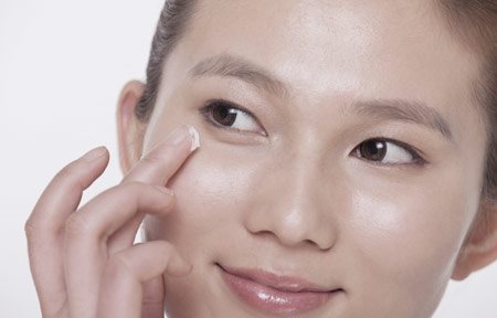 Asian woman applying cream under her eyes
