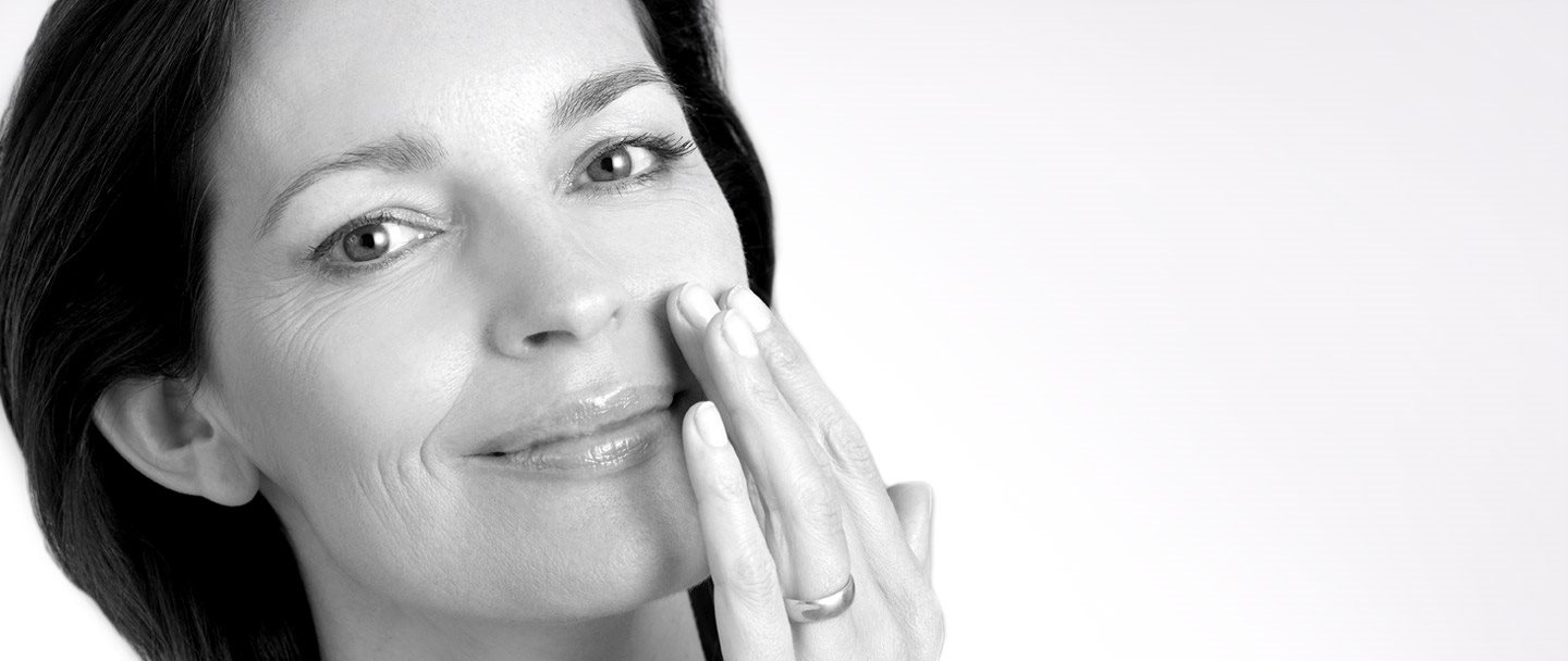 Middle-aged woman touching left cheek with hand.
