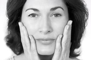 Middle-aged woman touching her cheeks with both hands.