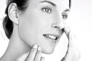 Woman applying cream on her cheek.